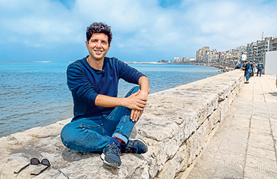 Jaafar Abdul Karim sitzt auf einer Stadtmauer vor dem Mittelmeer