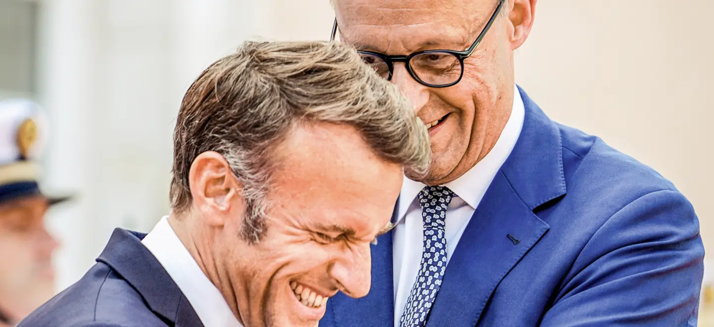 Die Staatschefs Emmanuel Macron und Friedrich Merz lachen gemeinsam.