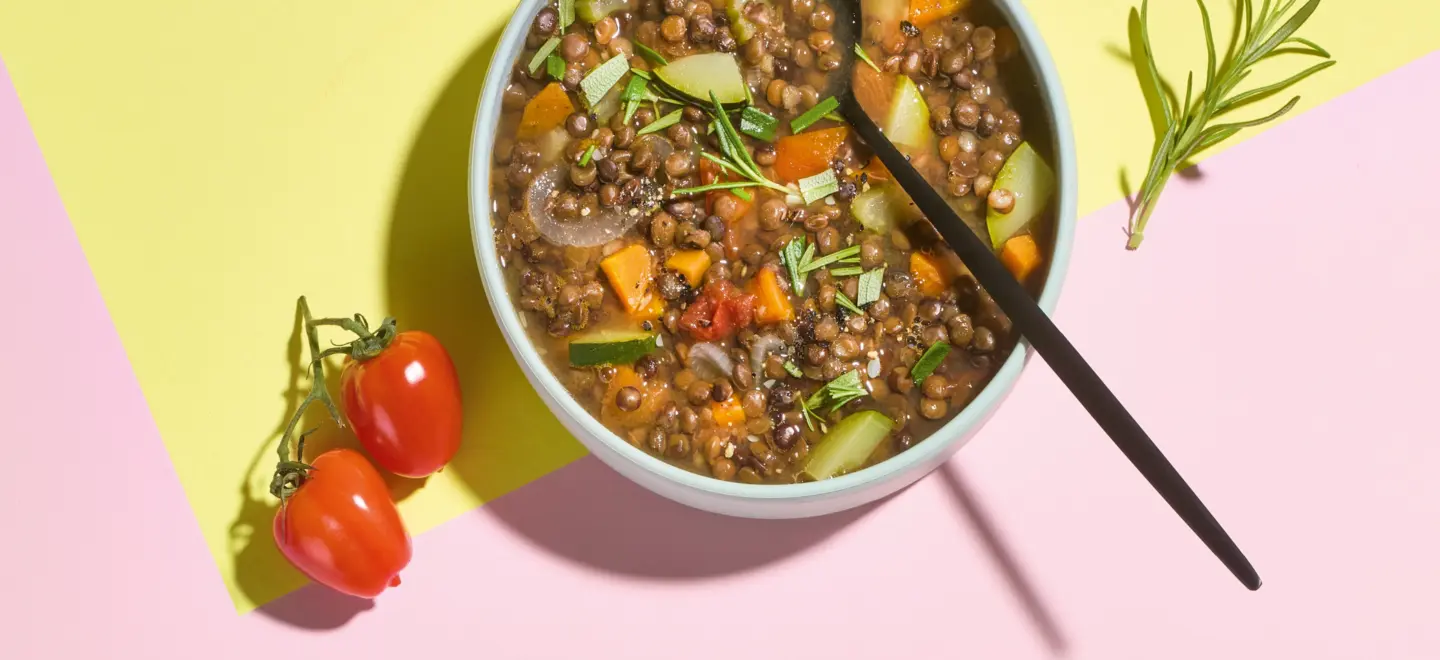 Linsensuppe auf buntem Hintergrund mit Tomaten und Kräutern