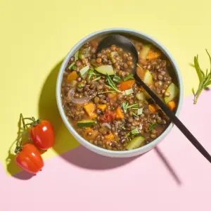 Linsensuppe auf buntem Hintergrund mit Tomaten und Kräutern