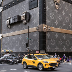 Louis Vuitton Koffer in Übergröße als Werbung an einer Kreuzung in New York, davor gelbe Taxen